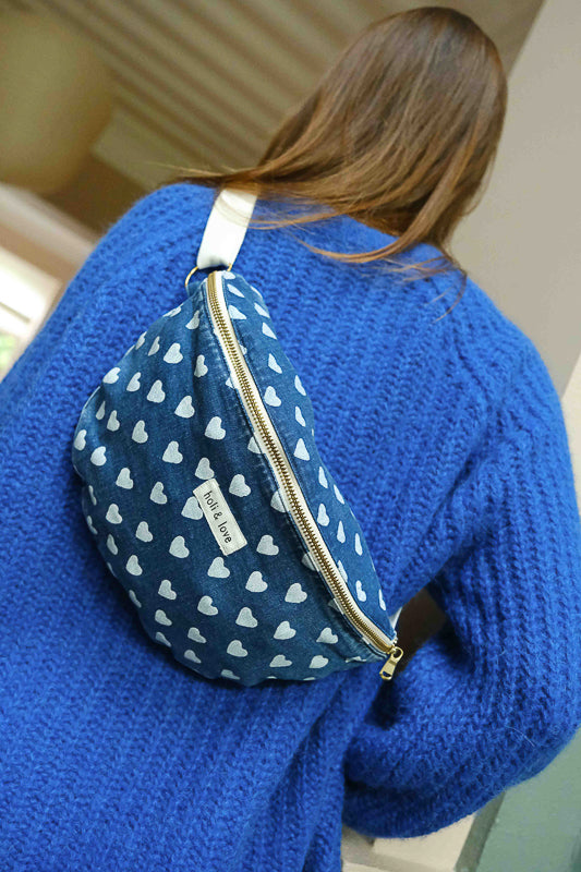 Sac banane porté par une femme, imprimé cœur sur tissu en denim. Grand sac pour femme à porter en bandoulière.