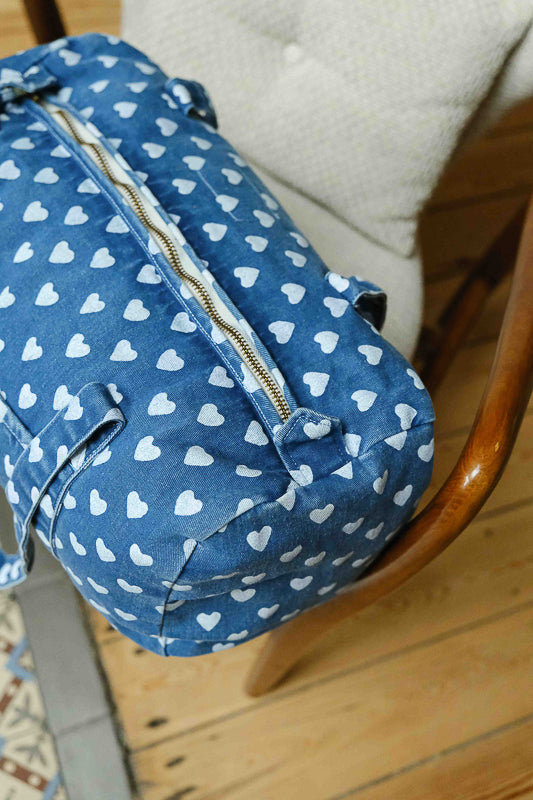 Détail du tissu et de la fermeture du sac weekend en denim imprimé cœurs. Sac de voyage et accessoire de mode pour femme en coton.